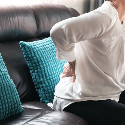 Woman leaning forward on couch with hand on lower back